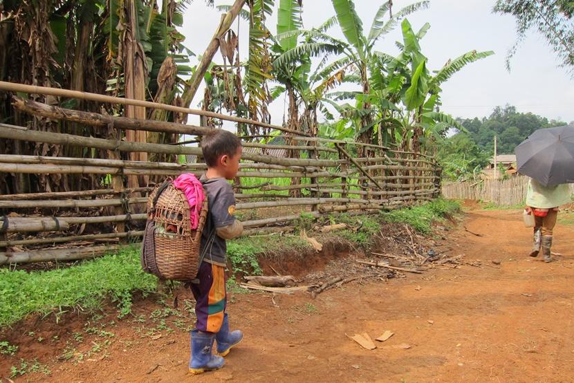 A boy walks down a dusty road carrying a backpack Laos boy walking down road with backpack