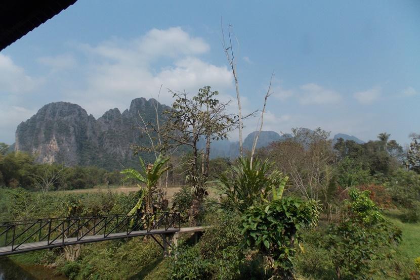A green landscape with a bridge and cliffs in the distance A bridge across the water with a mountain in the background