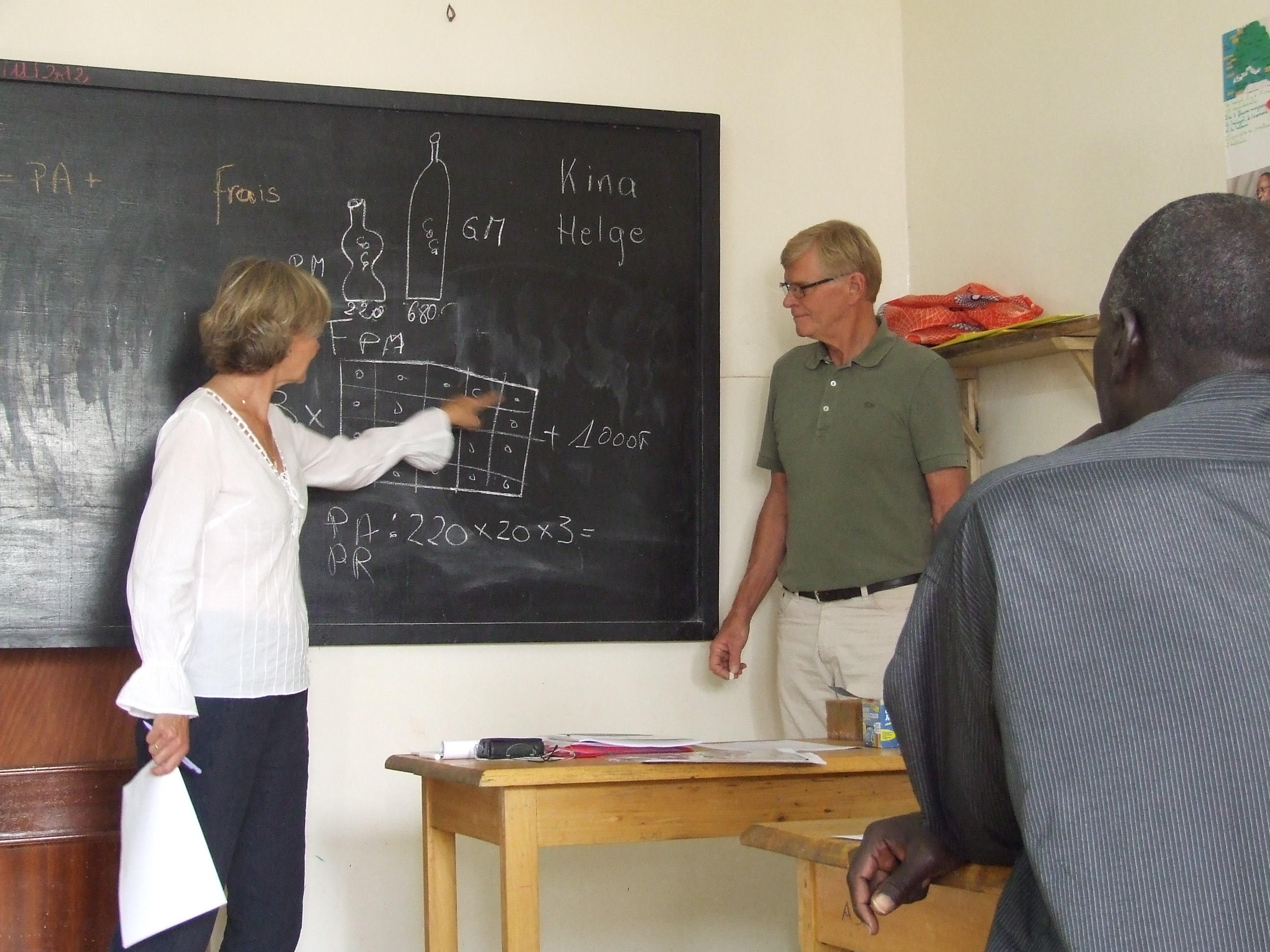 Two older people volunteering in Africa teach a maths class at a Micro-finance Project. Students in Africa attend a maths class taught by older adults volunteering abroad on a Micro-finance Project.