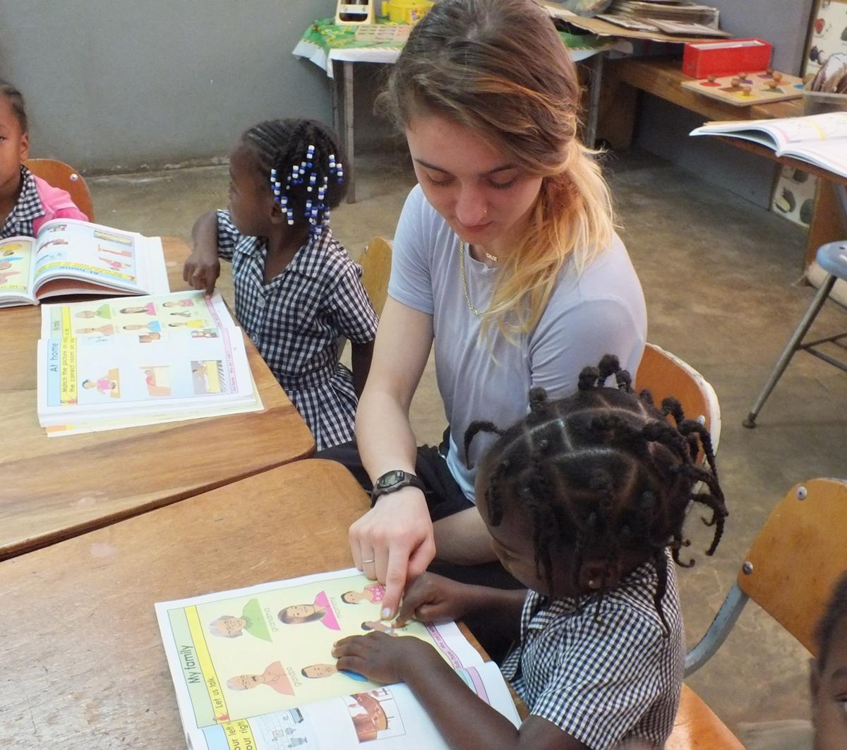 A teenage volunteer works at a summer camp in Jamaica as part of a High School Special A teenage volunteer abroad for the first time helps a young girl read a book at a summer camp in Jamaica