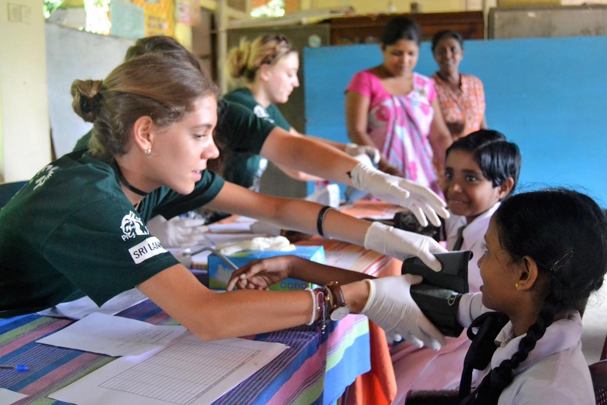 A High School Special volunteer works at a medical outreach in Sri Lanka on their first trip abroad. Teenagers volunteering overseas for the first time check young children’s blood pressure in Sri Lanka.